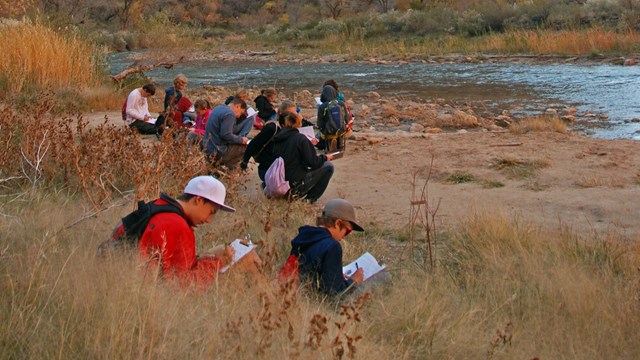 A group of students writing in notebooks in the banks of the river