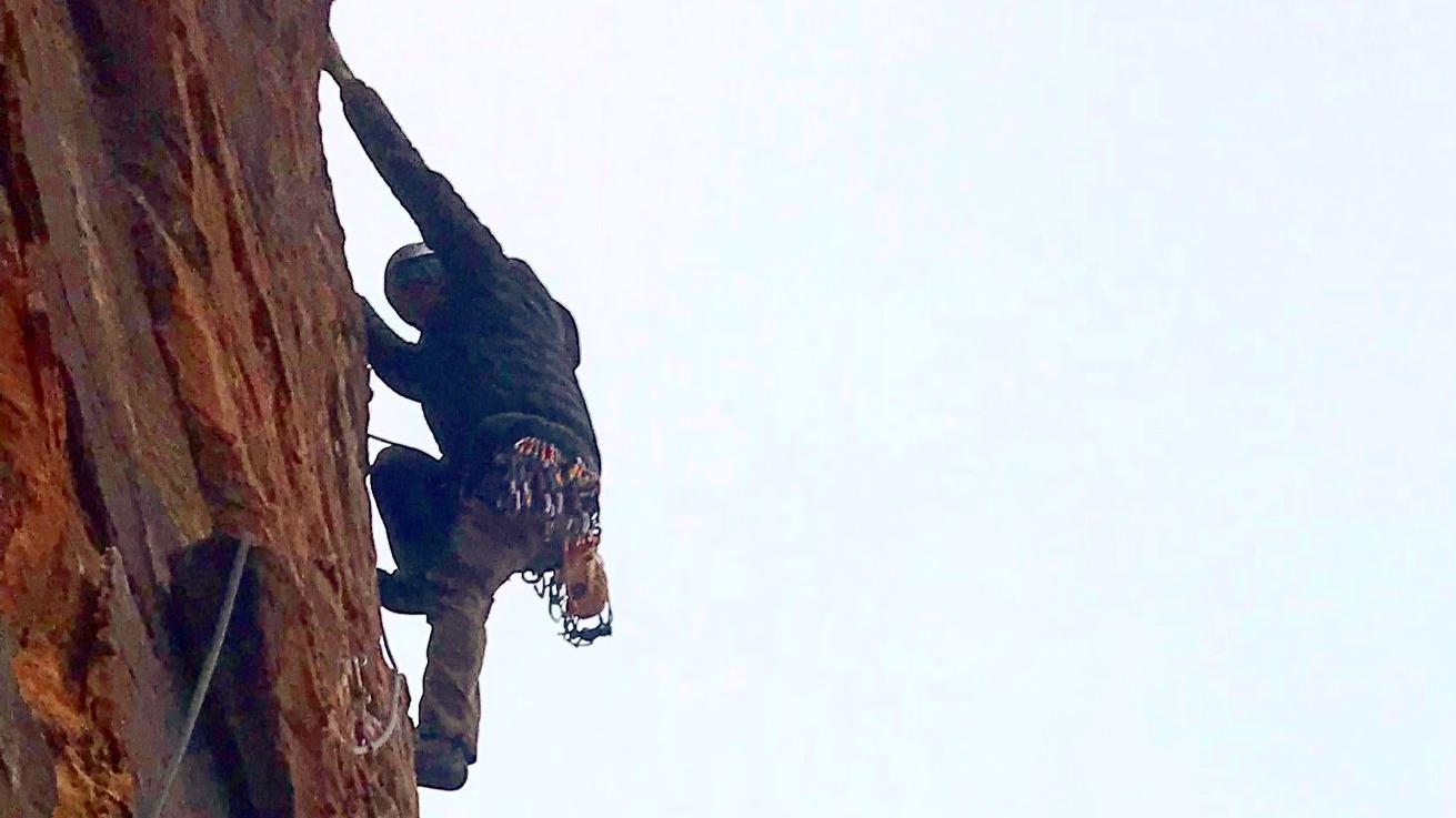 A person climbs up a steep canyon wall using ropes and anchors.