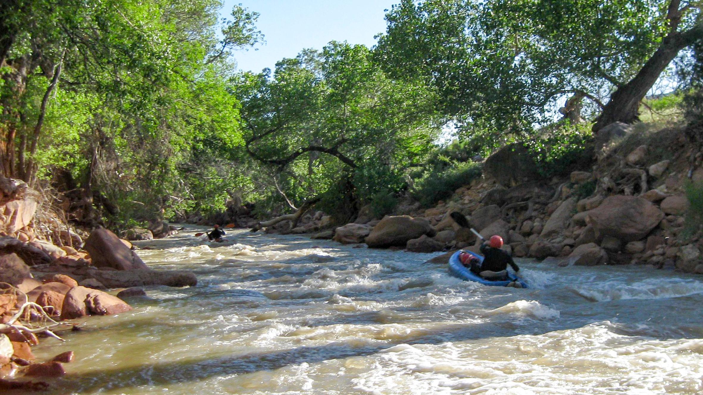 Two people in inflatable watercraft ride down the rapids of the Virgin River.