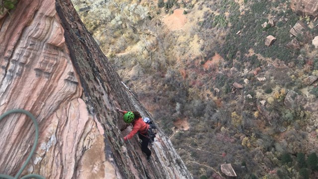 A climber scales a vertical wall high above the canyon floor.