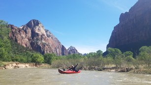 Visitors float down a river between towering canyon walls in an inflatable kayak.