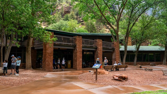 Zion Lodge stands among trees, with tall sandstone cliffs in the background.