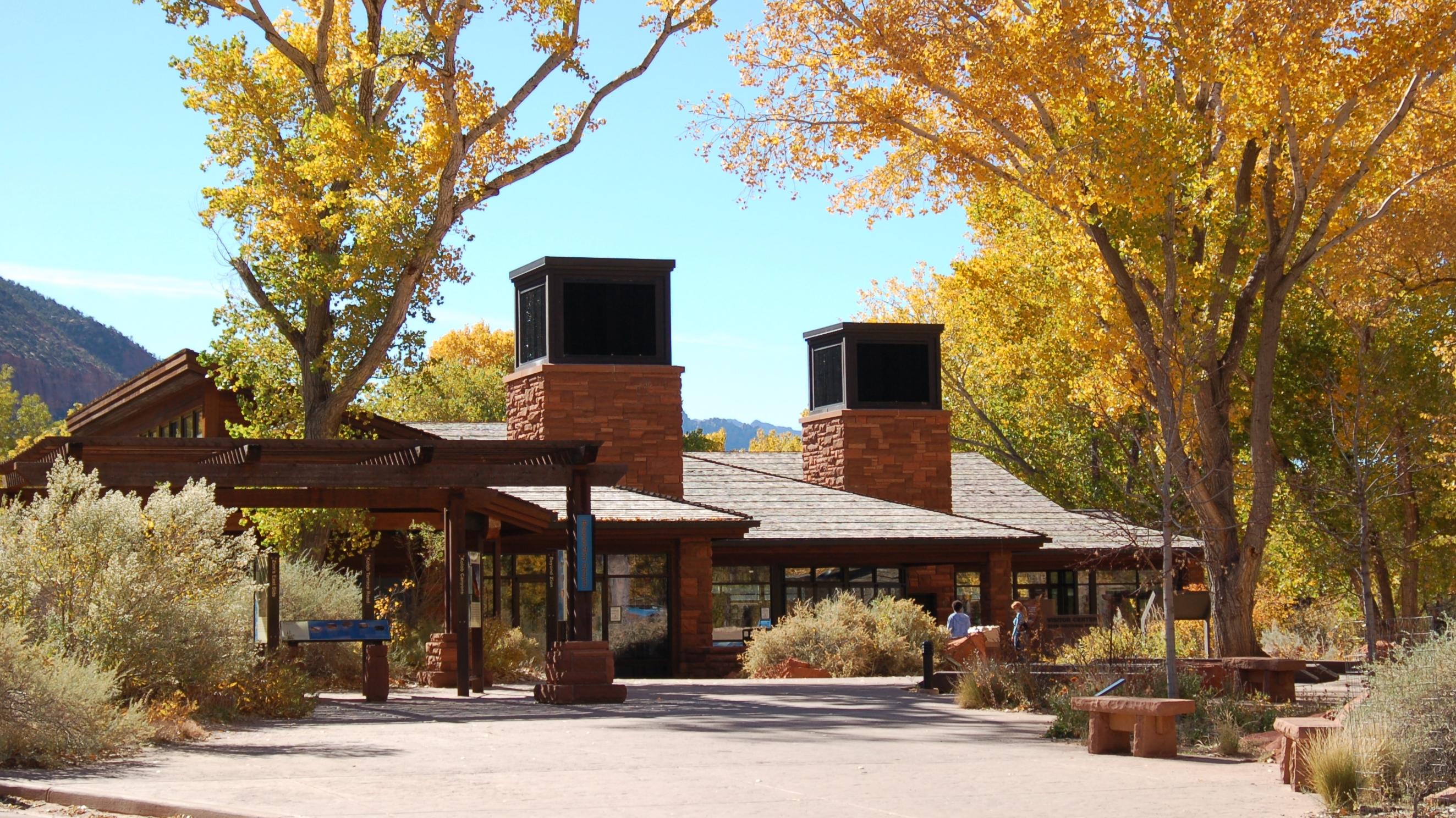A visitor center building with two large swamp cooler towers. Yellow trees stand in front.