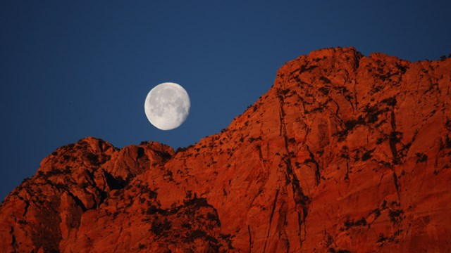 A full moon above red cliffs