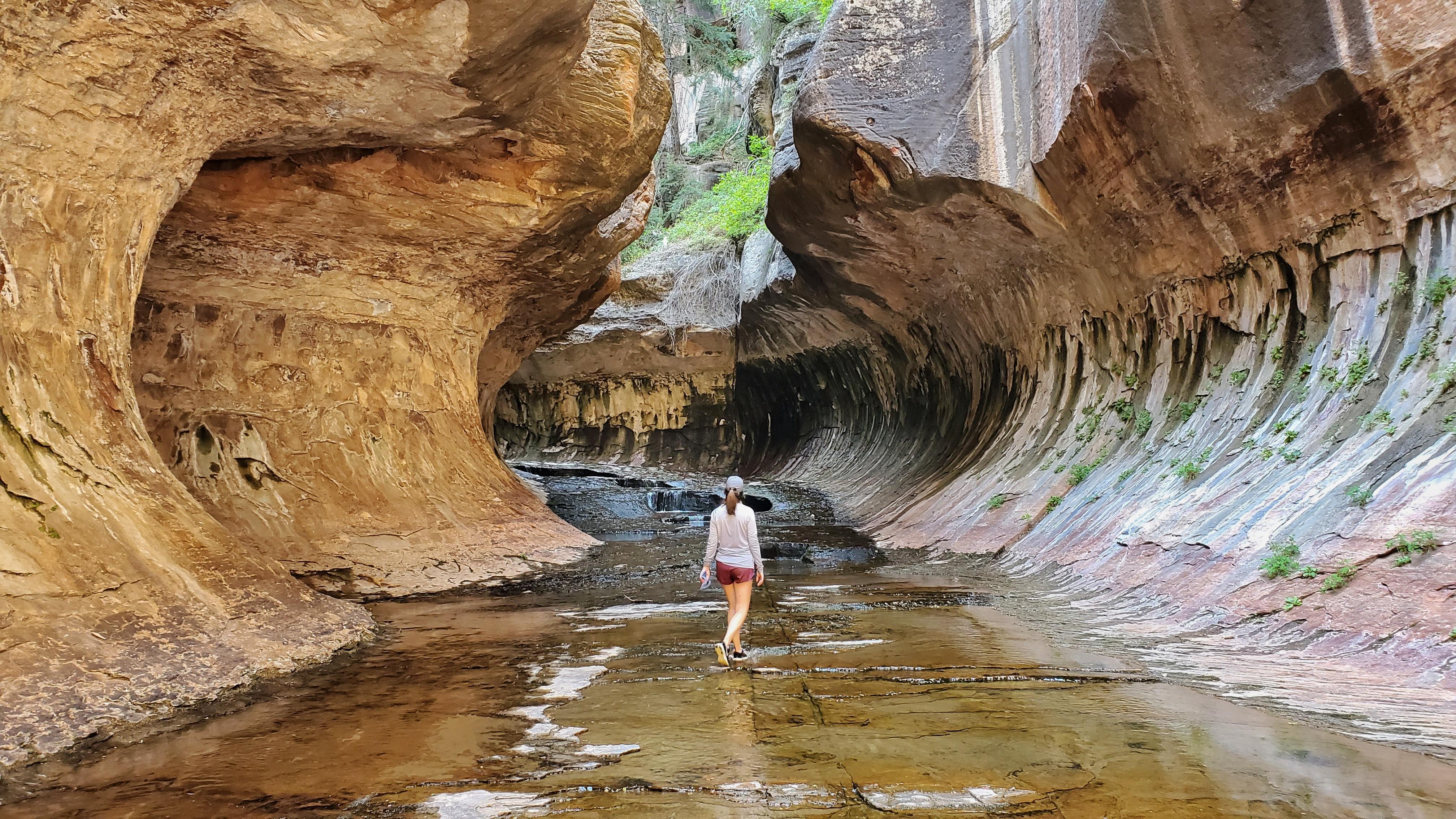 A hiker walks through a creek in a slot canyon.