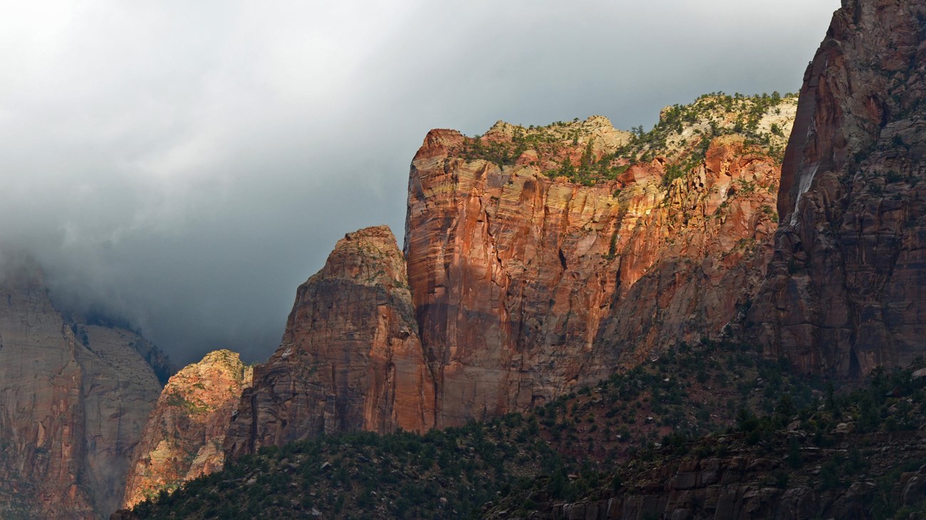 A man in a bright green swiftwater rescue outfit stands by a flooding river.