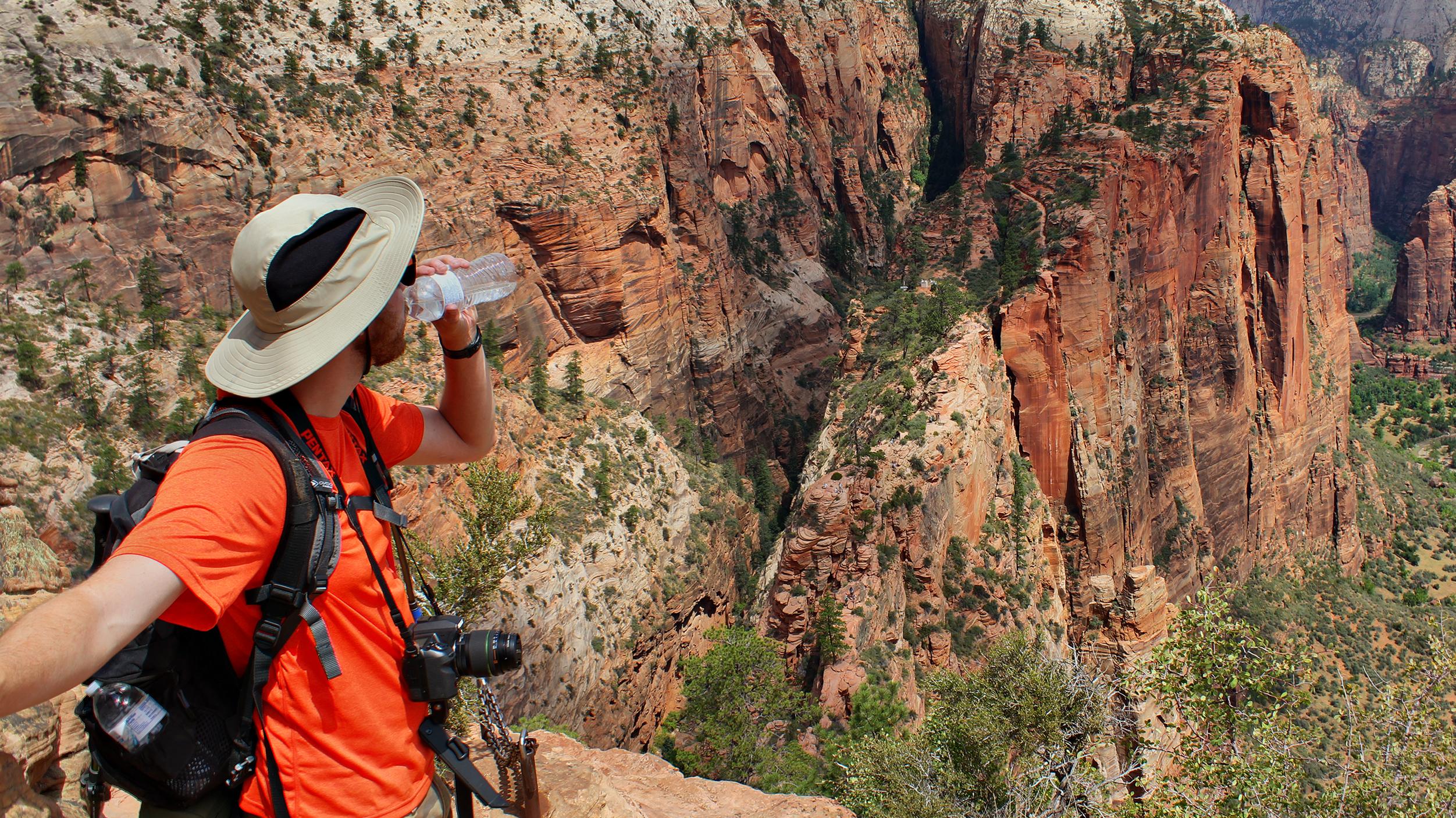 A hiker holds drinks water as they gaze into Zion Canyon.