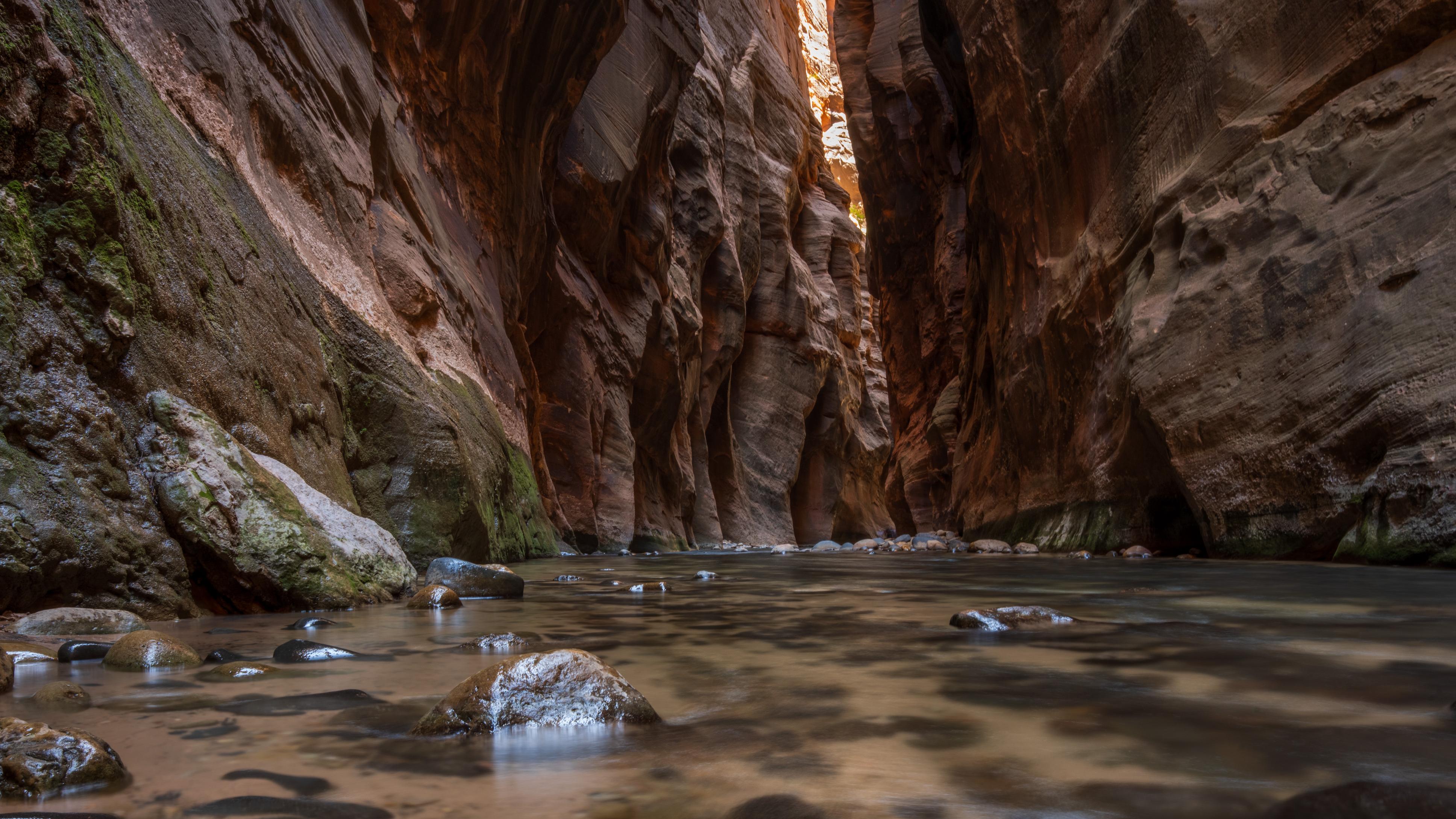 A tall and narrow canyon, only about 30 feet wide. Shallow water runs along the bottom.