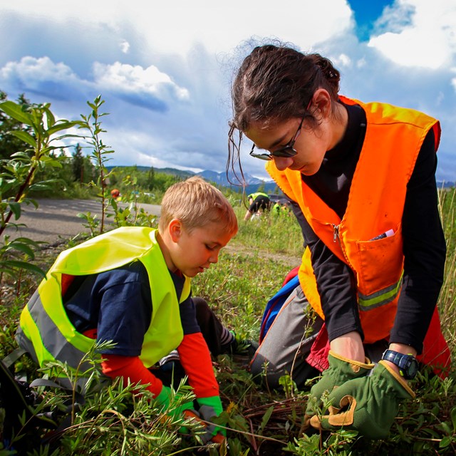 a young boy and girl in safety vests pull weeds