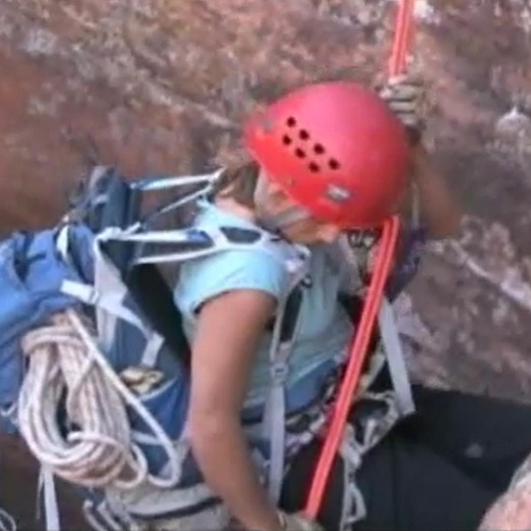 A canyoneer wearing a helmet and backpack rappels down into a canyon.
