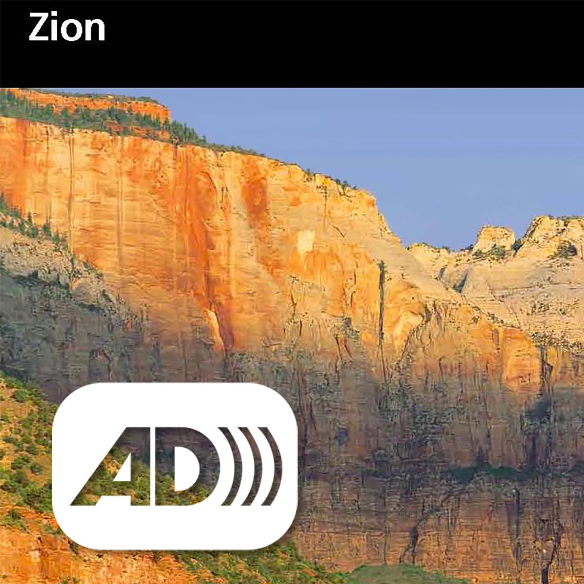 Zion unigrid with blue sky over sandstone mountains. Audio description symbol in corner. 