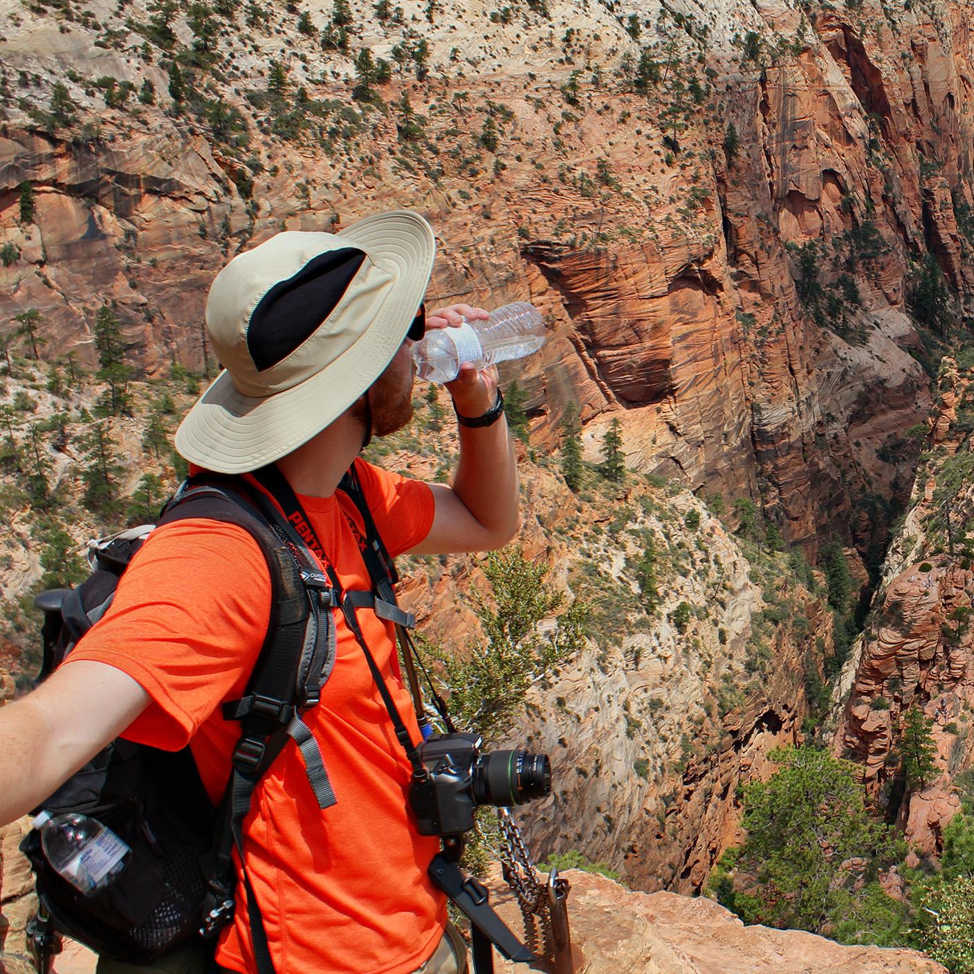 A hiker drinks water from a bottle as they gaze into Zion Canyon.
