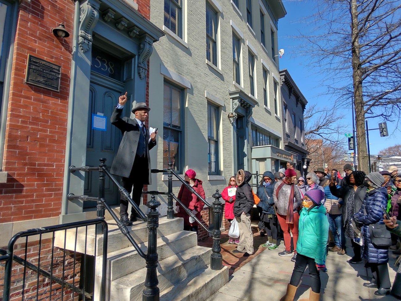 Wallace is on the steps with his hand raised. The crowd of people are standing around him.