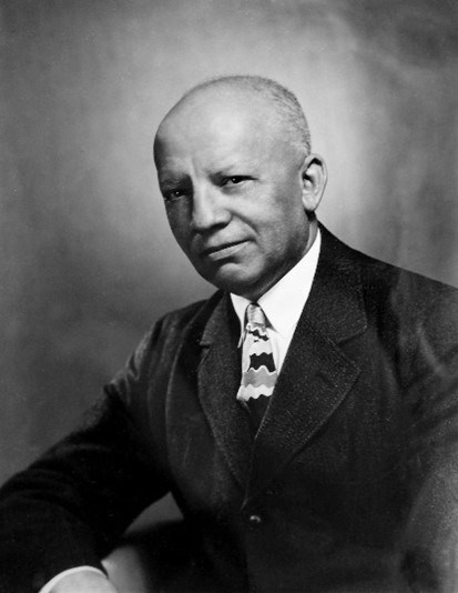 A black and white headshot of Dr. Carter G. Woodson. 