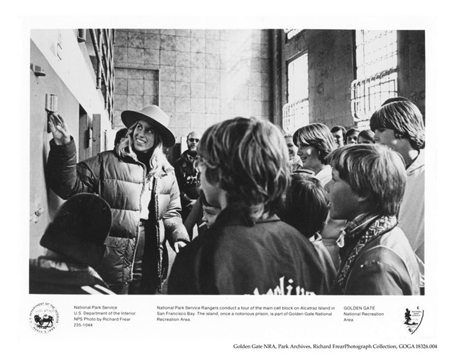 Black and white photo of a smiling female ranger with long hair and a flat hat pointing to part of t