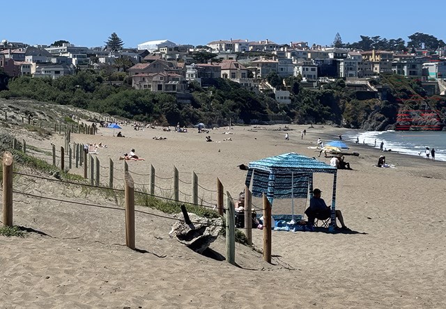 People sit on a beach with houses in the background