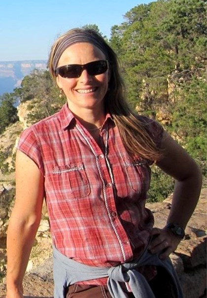 Smiling woman with red plaid shirt in front of mountain, rocks, trees