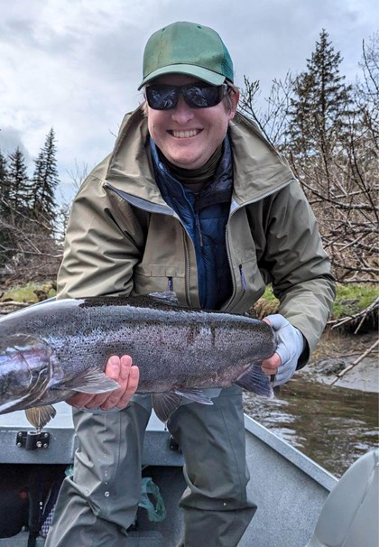 Smiling man holding large silver fish in boat on river with muddy banks
