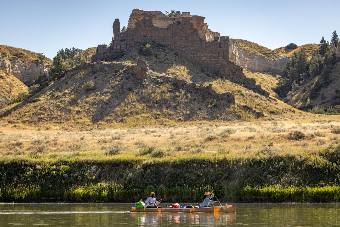 Two people in a canoe paddling with rock formations above