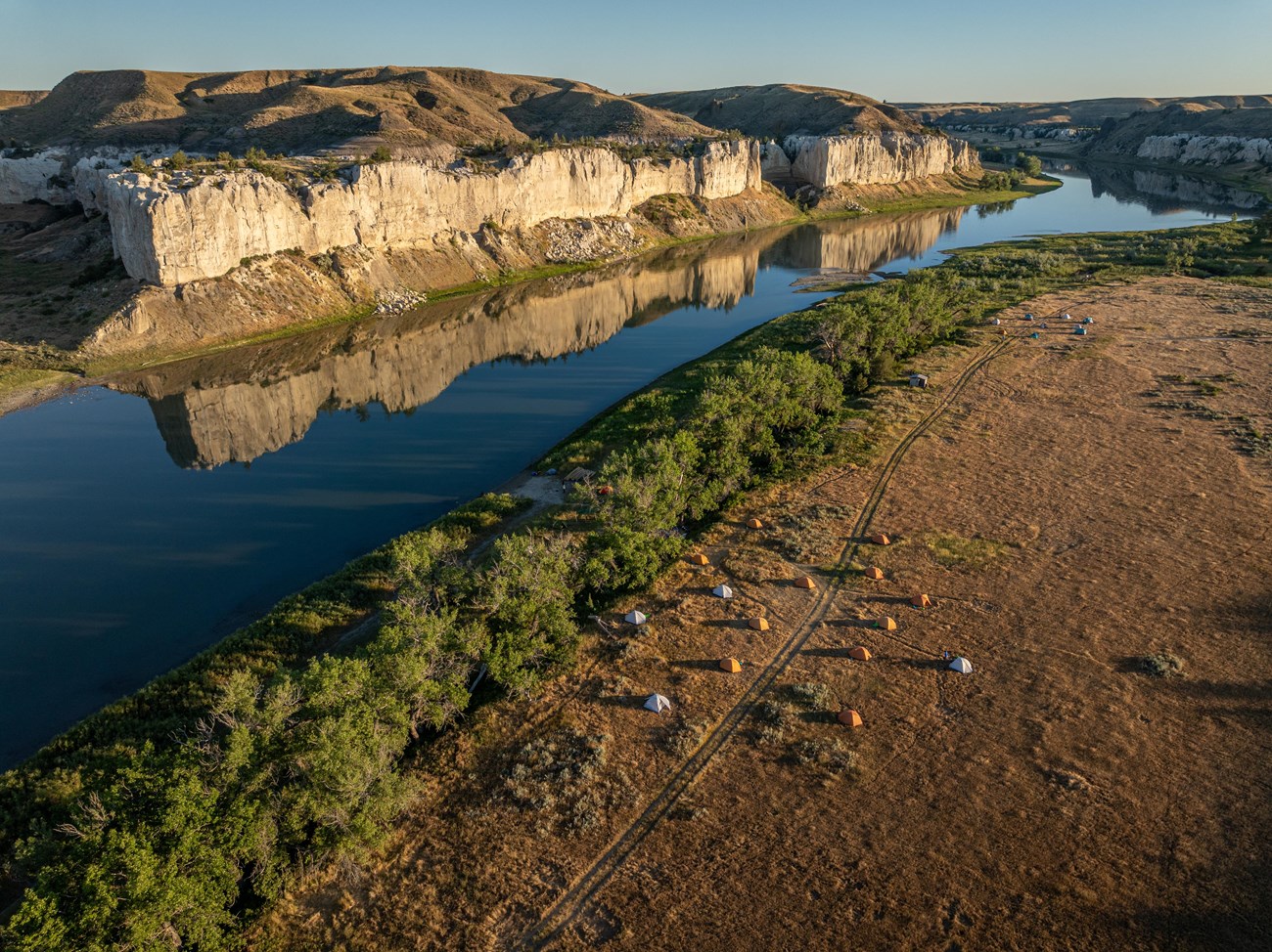 Aerial drone image of tents along a winding river, with white cliffs reflected in the glassy water