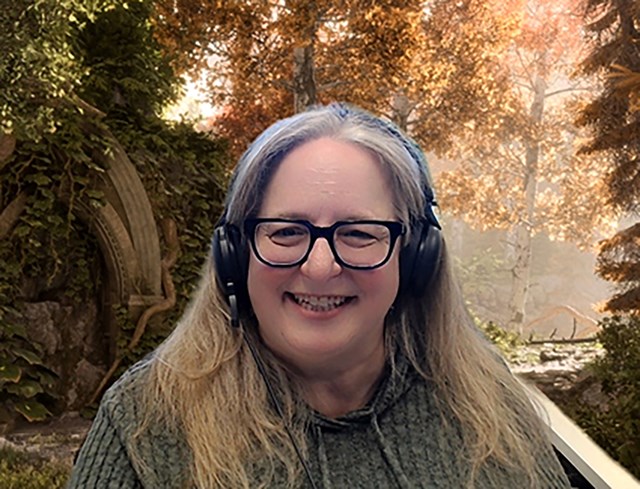 Smiling woman with long hair in front of a woodland background