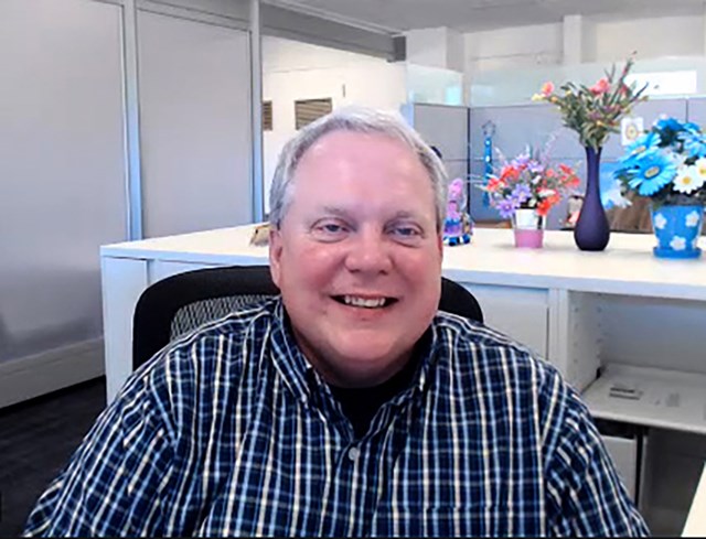 Smiling man in blue plaid shirt in front of an office background