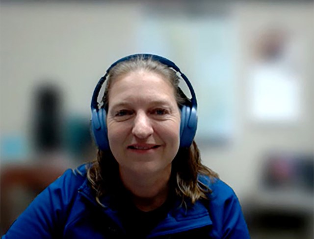 Smiling woman with headphones and royal blue garment in front of a blurred background