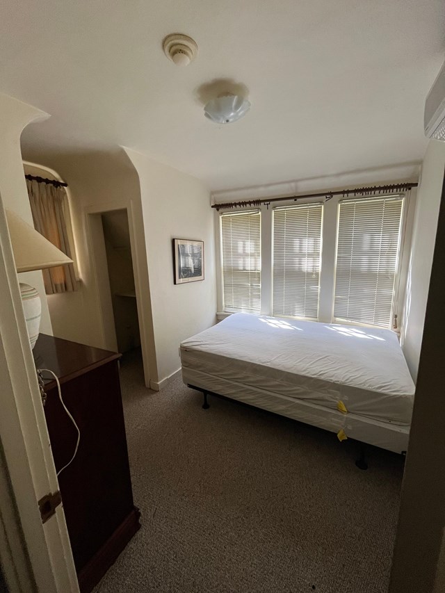 a bedroom with a bed, small closet, a dresser and lamp, and a row of three windows