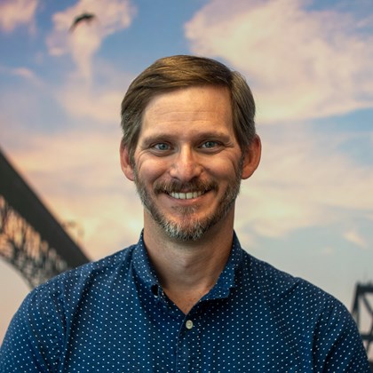 Headshot Photo of Brent Everitt with a bridge and clouded sky background.