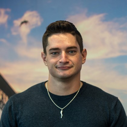 Headshot Photo of Seth Orcutt with a bridge and clouded sky background.