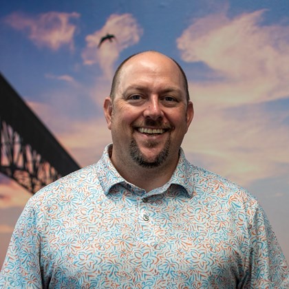 Headshot Photo of Joel Cadoff with a bridge and clouded sky background.