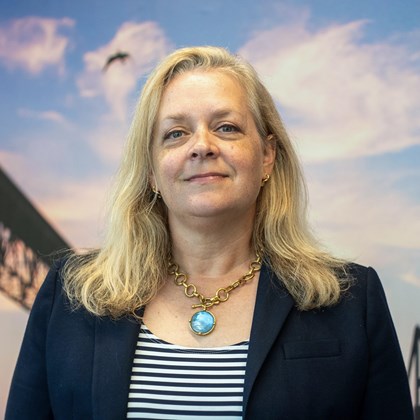 Headshot Photo of Kate Marks Hardy with a bridge and clouded sky background.