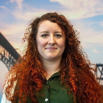 Headshot Photo of Samantha Utt with a bridge and clouded sky background.