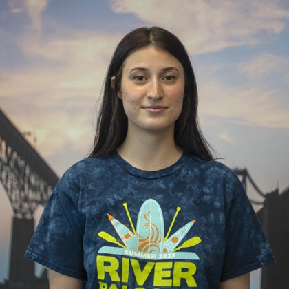 Headshot Photo of Dana Sanchez with a bridge and clouded sky background.