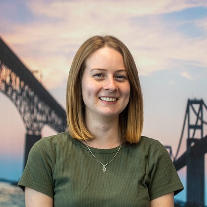 Headshot Photo of Sarah King with a bridge and clouded sky background.