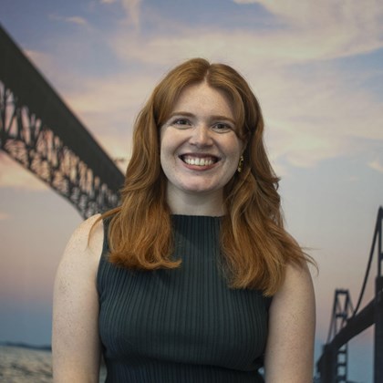 Headshot Photo of Lydia Heisel with a bridge and clouded sky background.