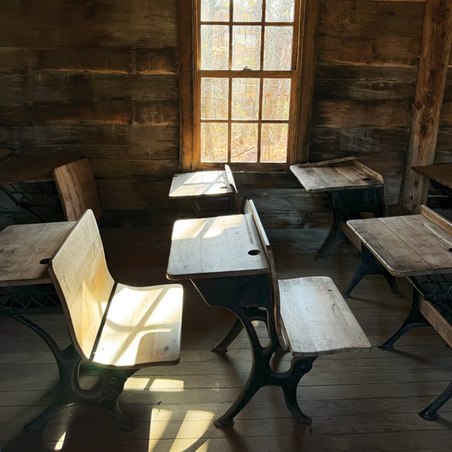 Interior of the historic Hensley Settlement schoolhouse showing wooden student desks and chairs.