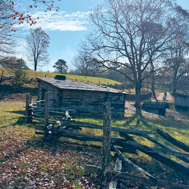 A log cabin surrounded by split-rail fencing and a field.