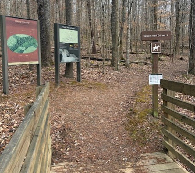 Wooden bridge in the front then two panel signs and a horse riding trail post.