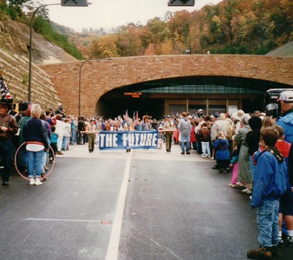 Large groups of people celebrating opening day as a parade of people come through the tunnel.