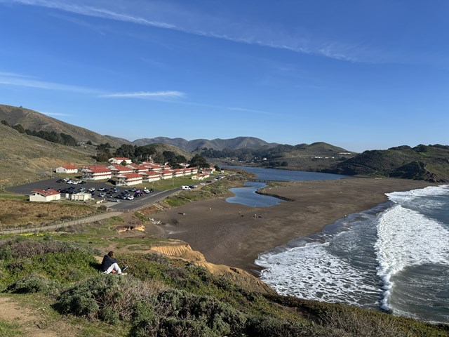 Waves crash on a beach near a series of barracks buildings.