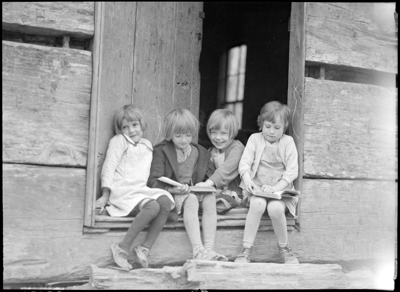 Four children sitting on a schoolhouses steps. 