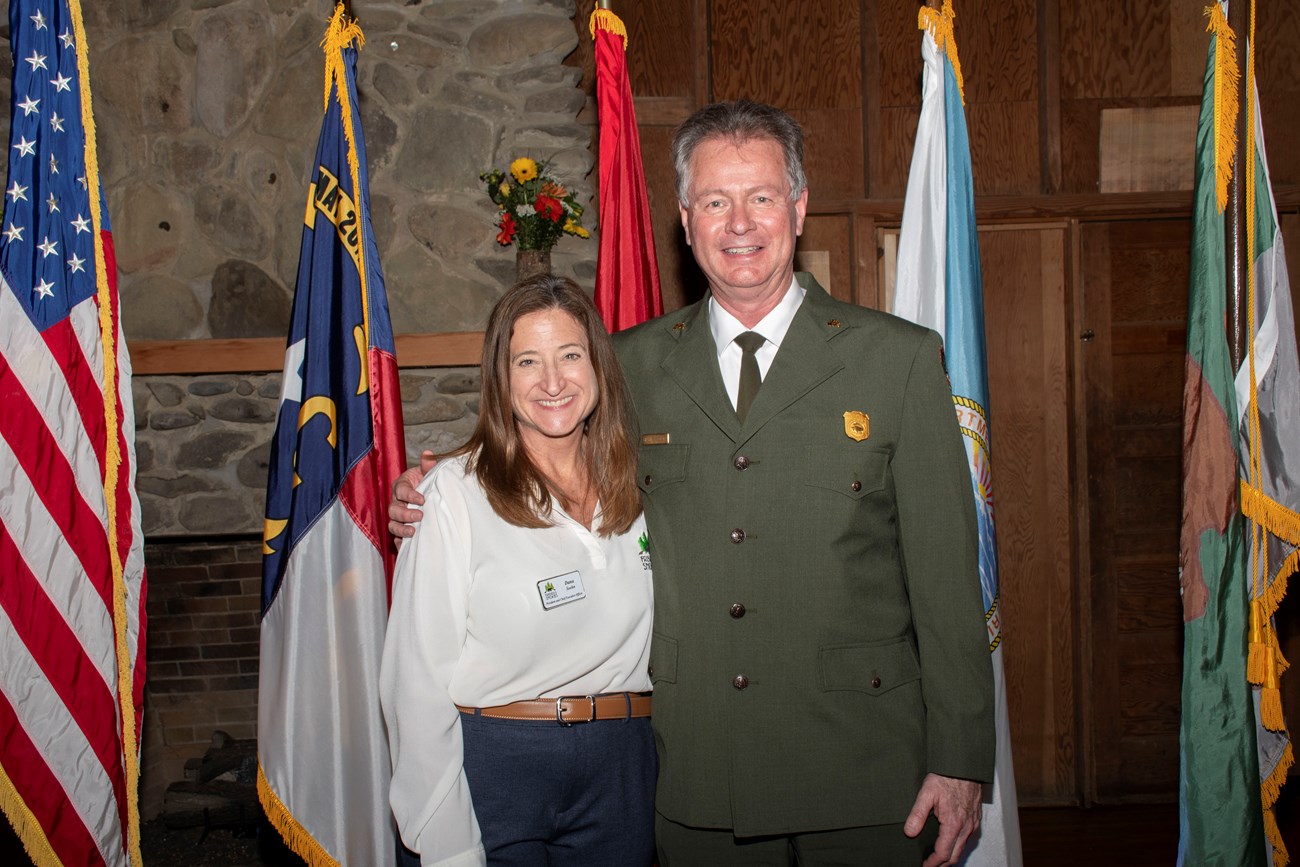 A lady and a ranger take a photo in front of standing flags.