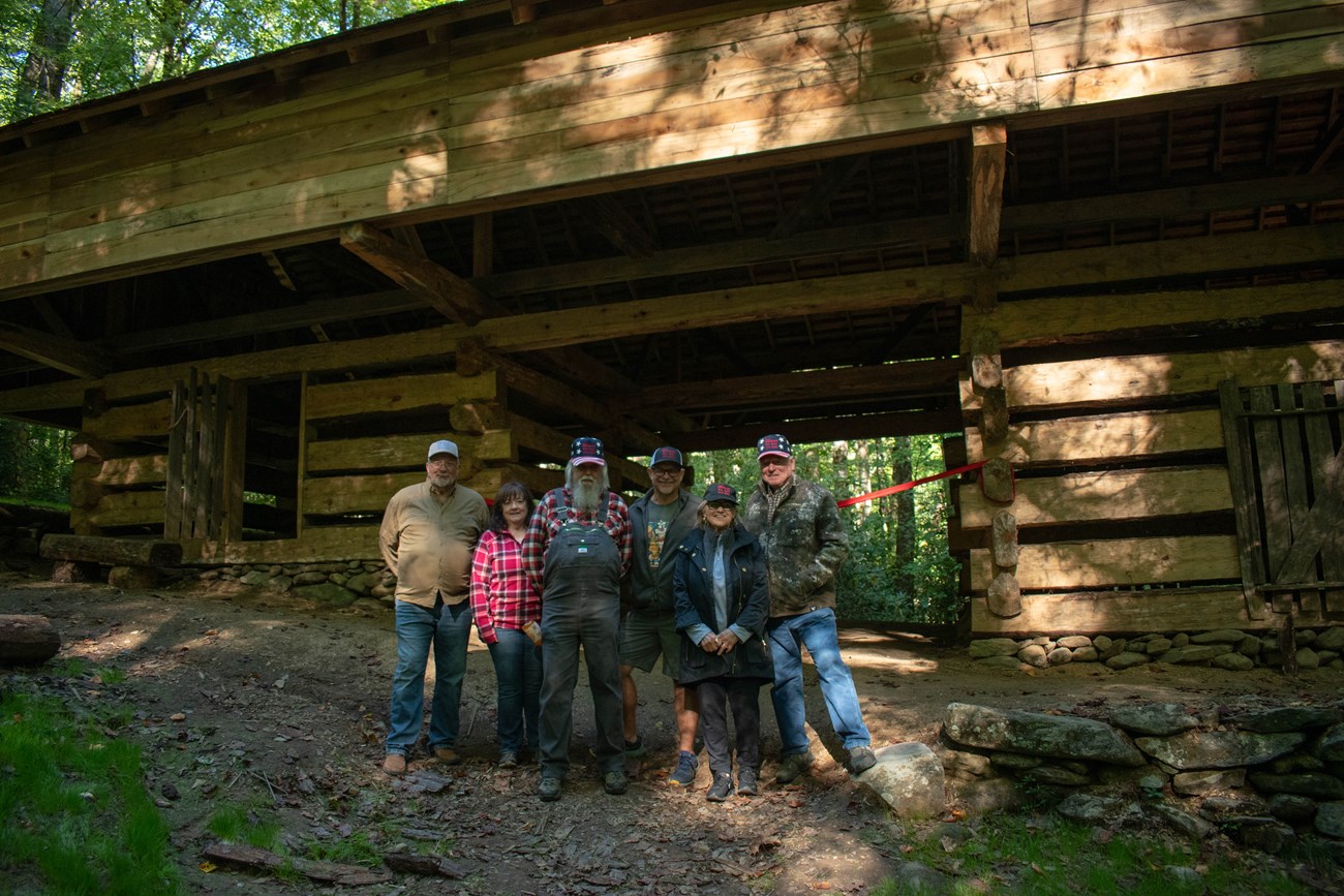 A group of people in matching hats stand in front of a cantilever barn.