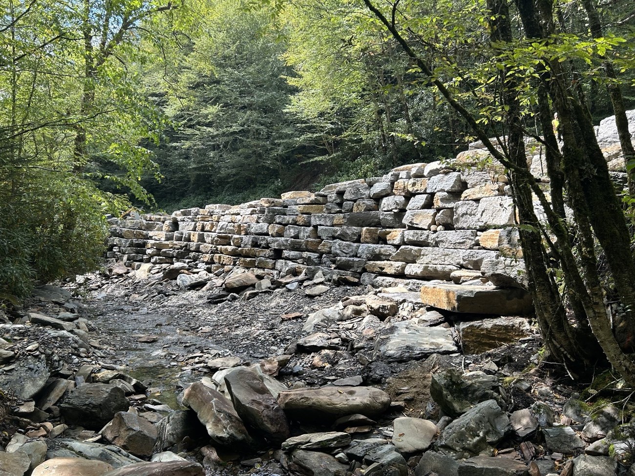 A stone retaining wall beside a stream.