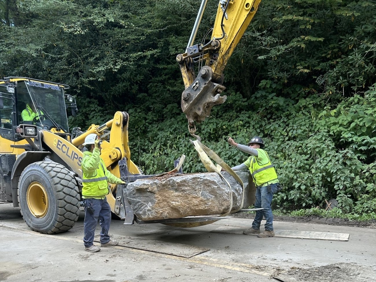 Two workers and a tractor moving a large rock.