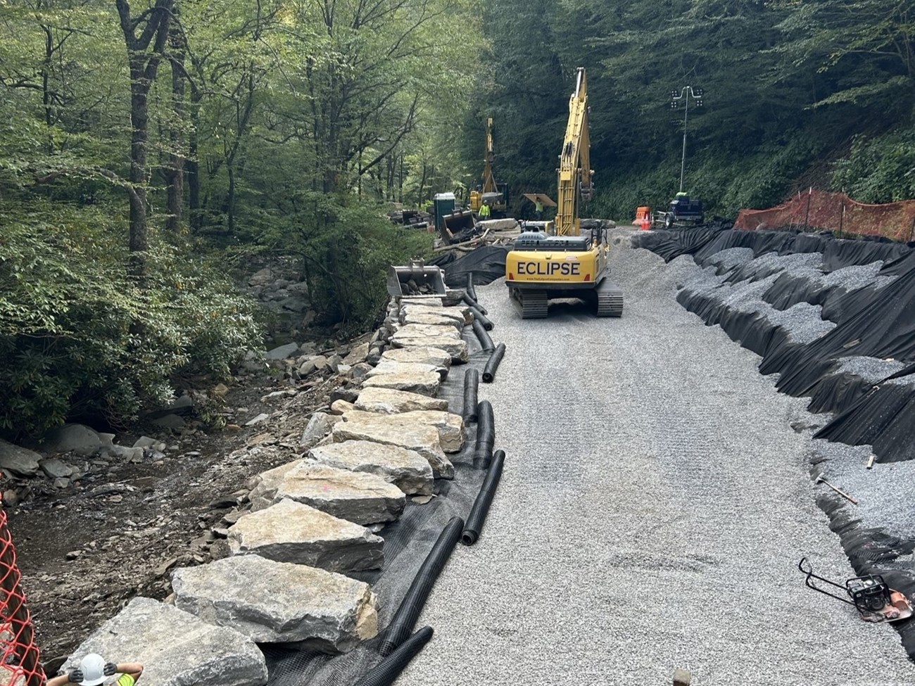 Equipment on a new gravel filled road in the forest along a stream.