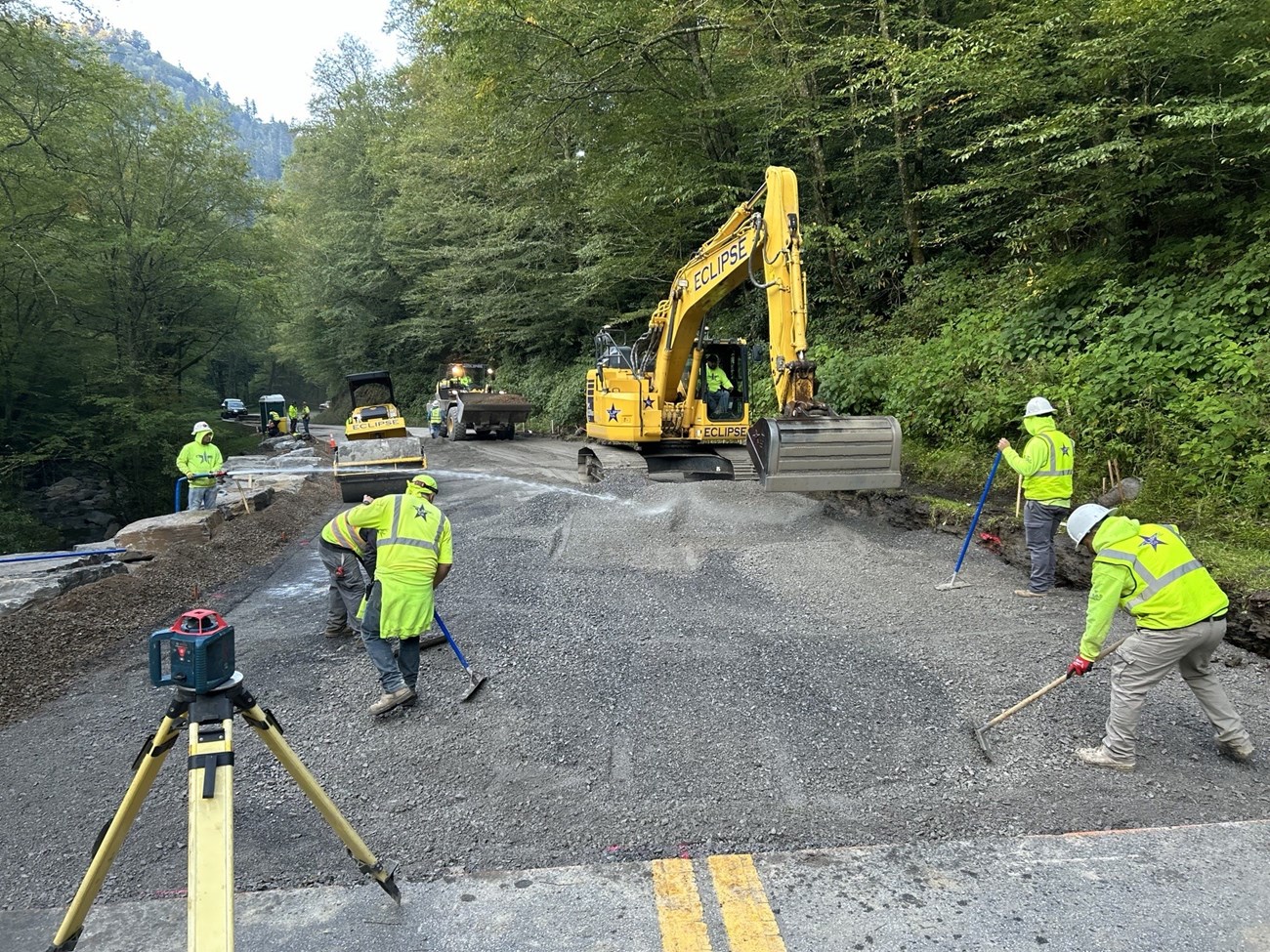 Crew filling in gravel on a new roadway in the forest.