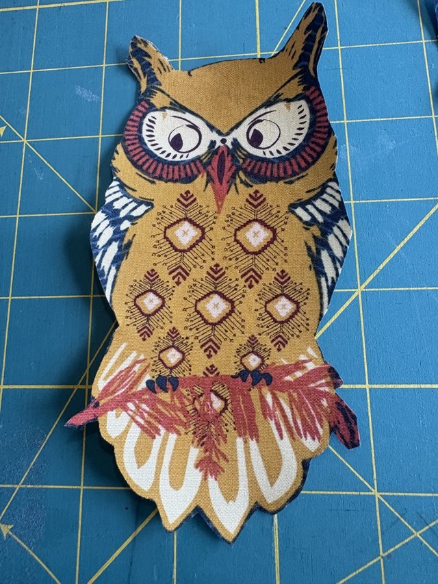 An owl cutout of fabric on a blue cutting board.