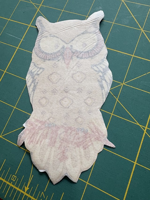 An owl cutout of fabric slipped over on a green cutting board.